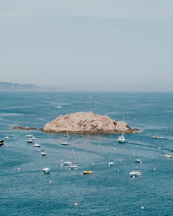 Aerial Photography Of A Rock Island Surrounded by Sea Vessels