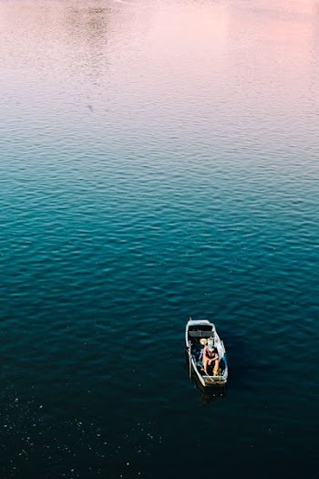 aerial photography of person sitting on boat on calm body of water