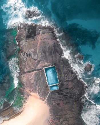 Aerial Photography of Teal and White House on Rock Formation Near Body of Water