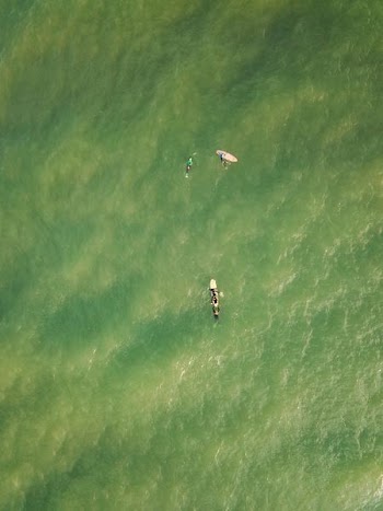 aerial photography of three person on surfing board floating above body of water