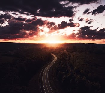 aerial view of a road surrounded by trees during sunset