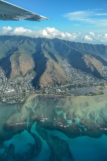 aerial view of sea beside mountains under blue and white cloudy sky