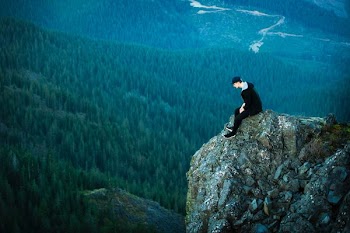 aerial view photography on man sitting on cliff
