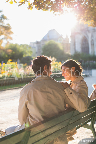 Affectionate couple talking on sunny park bench