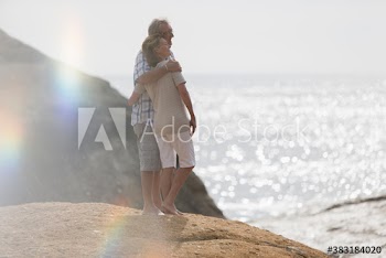 Affectionate senior couple hugging on sunny beach rock