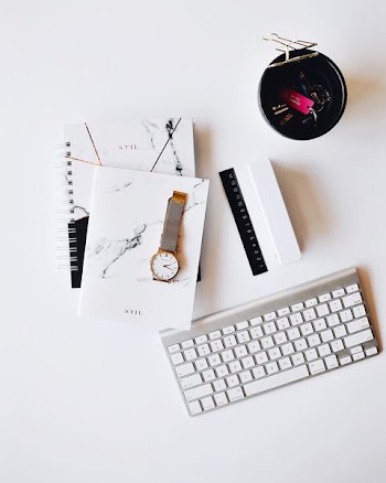 Apple Magic Keyboard near round gold-colored analog watch with silver-colored mesh band with notebook on white surface photography