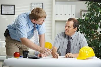 Architects working at office - planning and talking over blueprint on desk.