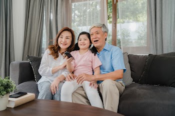 Asian grandparents watch tv with granddaughter at home. senior chinese, grandfather and grandmother happy using family time relax with young girl kid lying on sofa in living room concept. Free Photo