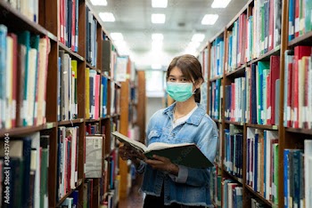 Asian university student girl wearing face protective medical mask for protection from virus disease reading book at library. Education, high school, university, learning and people concept