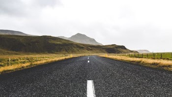asphalt road in the middle of field along mountain
