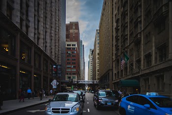 Assorted Vehicles on Road Beside High-rise Buildings Across Towers Under White and Blue Cloudy Skies