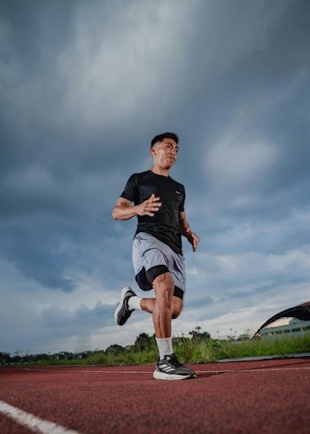 Athletic Young Man Running on Track under Dramatic Sky
