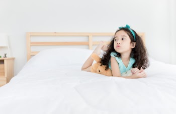 attractive asian children rest on white bed, pucker lips, she feeling happy, curly hair