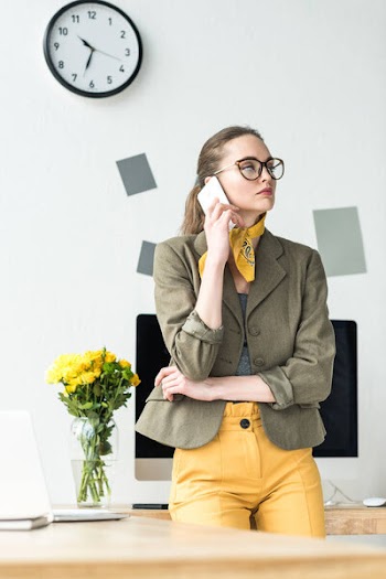 Attractive businesswoman in eyeglasses talking by smartphone and looking away in office