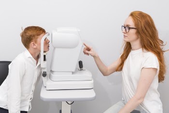 Attractive female ophthalmologist checking boy eyes with refractometer machine at optics clinic Free Photo