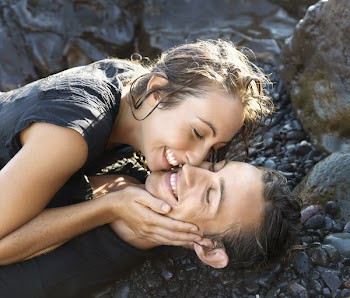 Attractive young couple smile with closed eyes while lying on a rocky shore. Vertical shot.