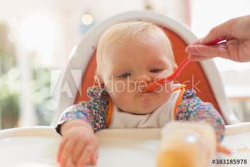 Baby girl being fed by spoon in high chair