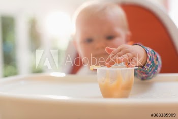 Baby girl in high chair reaching for baby food