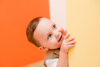 baby hiding beside beige wall