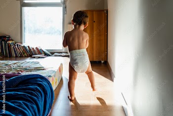 Baby in diapers learning to walk in her bedroom barefoot.