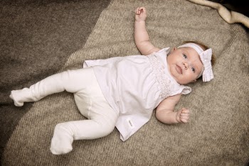 Baby in White Dress Laying on Gray Textile