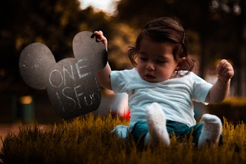 Baby Wearing Blue Shirt Holding Mickey Mouse Head Cutout Sitting on Grass