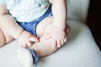 Baby Wearing Green Shirt and Blue Shorts Sitting on Gray Chair