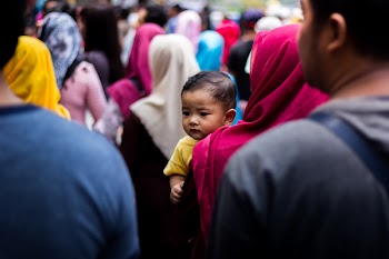 Baby Wearing Yellow T-shirt on Woman's Arm in Crowd
