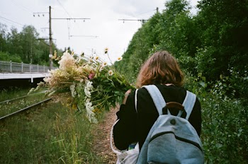 Back view photo of a person wearing a backpack and  holding flowers