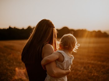 Back view photo of a woman in black sleeveless top carrying a toddler