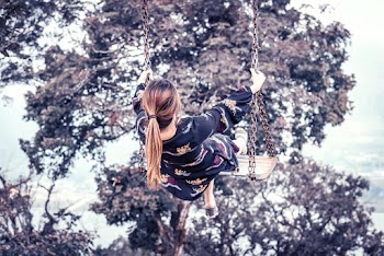 Back view photo of a woman on swinging near a tree 