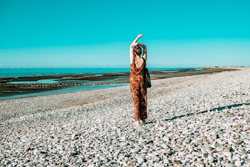 Back view photo of a woman wearing orange and black floral sleeveless jumpsuit standing on seashore
