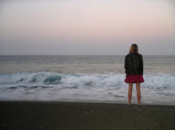 Back View Photo of Barefoot Woman in Black Leather Jacket and Standing by the Beach Looking at the Horizon