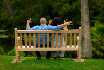 Back View Photo of Couple Sitting on Brown Wooden Bench Holding Out Their Hands Spelling The Word Love With Their Fingers