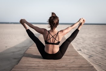 Back View Photo of Flexible Woman Sitting on Wooden Footpath by the Beach Stretching