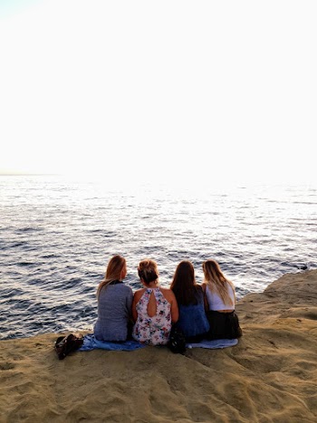 Back view Photo of Four Woman Sitting on the Seashore