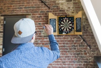 Back View Photo of Man in  Blue Dress Shirt  and Gray Hat Playing Darts