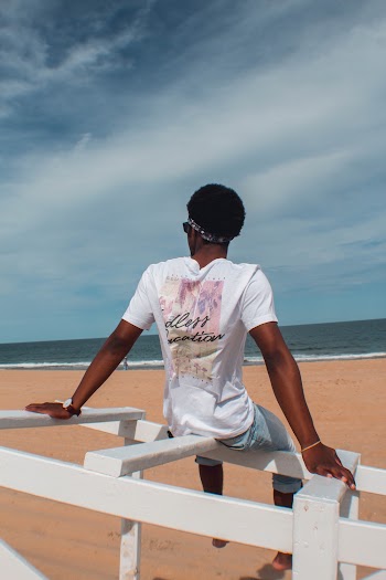 Back View Photo of Man Sitting on White Wooden Railing at The Beach