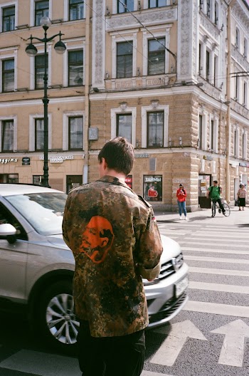 Back View Photo of Man Standing on Sidewalk Looking to His Left Waiting to Cross the Road as Car Drives By