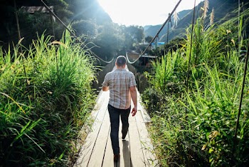 Back View Photo of Man Walking on Hanging Bridge