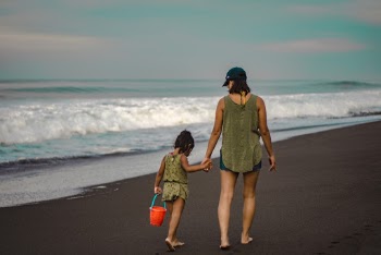 Back view Photo of Woman and Child Holding Hands While Walking on Beach