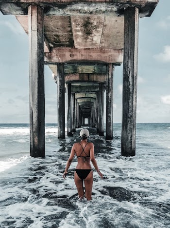 Back View Photo of Woman in Bikini Standing Below Wooden Oceanside Pier
