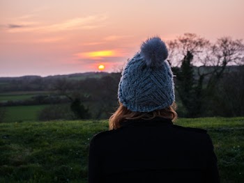Back View Photo of Woman in Blue Knit Cap Overlooking Golden Horizon