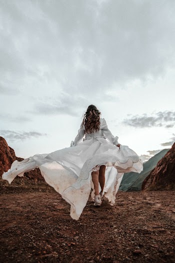 Back View Photo of Woman in White Dress Walking on Muddy Path