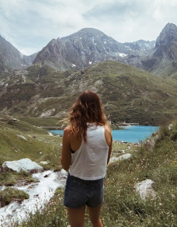 Back View Photo of Woman in White Tank Top and Blue Denim Shorts Overlooking Mountains