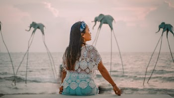 Back View Photo of Woman Sitting on Stone Railing By Seashore Looking to Her Right