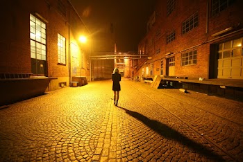 Back View Photo of Woman Walking Alone in the Middle of a Cobblestone Alley at Night
