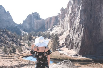 Back View Photo of Women in Black Floral Dress and White Sun Hat Overlooking Valley