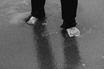 barefooted person wearing pants standing on wet sand