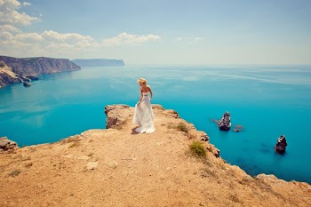 beautiful bride stands on the precipice of a blue sea